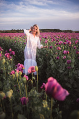 Beautifull happy woman with long hair in white dress lonely walking in the Lilac Poppy Flowers field