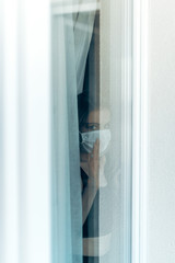 Woman with surgical protection face mask watching through window.