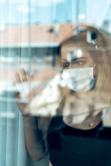 Woman with surgical protection face mask watching through window.