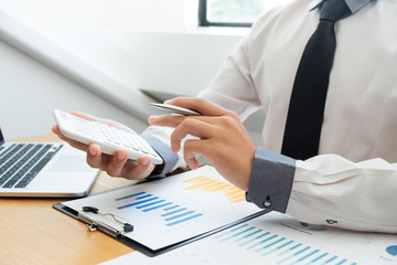 Business man are pressing the calculator to calculate the budget with business graph in the office.