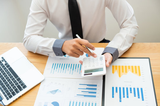 Business man are pressing the calculator to calculate the budget with business graph in the office.