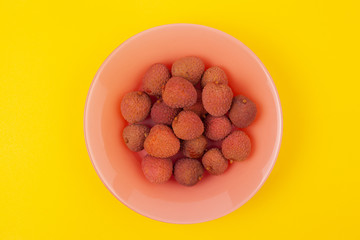 several lychee fruits lie on a coral plate on a yellow background