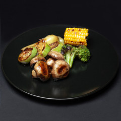 grilled vegetables on the grill on a black plate on a black background. corn, mushrooms, zucchini, broccoli.