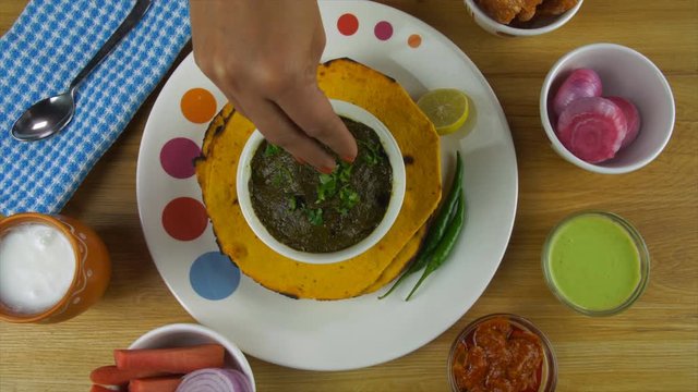 Top view shot of woman hands sprinkling chopped coriander leaves on Sarson ka saag . Closeup of popular Punjabi main course dish Makki ki Roti and saag served with Lassi  salad  pickle  mint chutne...