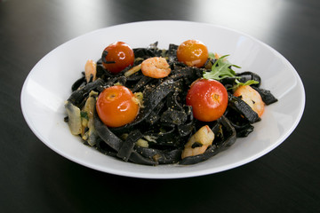 Italian cuisine - Fettuccine, spaghetti or tagliatelle al nero di seppia with seafood shrimps and cherry tomato in a dark wooden table