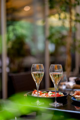 Two glasses of white wine with meal on summer terrace bokeh sunlight leaf cafe