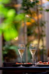 Two glasses of white wine with meal on summer terrace bokeh sunlight leaf cafe