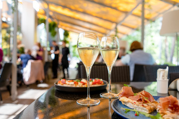Two glasses of white wine with bruschetts on summer terrace bokeh sunlight leaf cafe