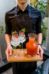 Waiter with Grapefruit lemonade with green and glasses on wooden board terrace bokeh