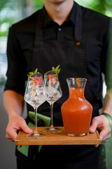 Waiter with Grapefruit lemonade with green and glasses on wooden board terrace bokeh