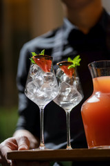 Waiter with Grapefruit lemonade with green and glasses on wooden board terrace bokeh
