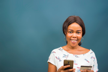 young beautiful african lady feeling excited about the transaction she carried out her cellphone, mobile phone, phone and holding her credit card