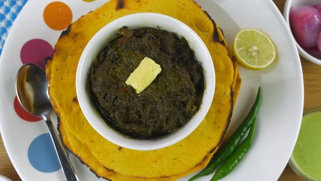 Traditional Punjabi cuisine Makki Ki Roti and Saag served in ceramic bowl and plate. Top view shot of popular north Indian Punjabi food Makki Ki Roti and Sarson ka Saag rotating on a turntable - wi...