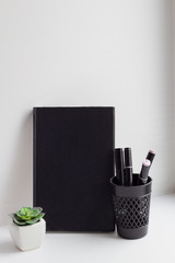 Office set consisting of a black notebook and stationery in a stylish black glass. Artificial succulent for decor is set nearby.