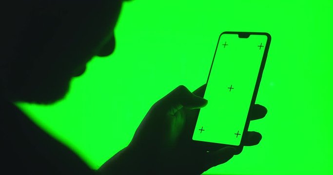 Silhouette of a man with a smartphone in his hands on a chromakey with a green background. Green screen smartphone for keying. Screen in tram chroma key smartphone technology cell phone touch display 