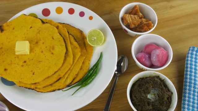 Pan shot - Punjabi Thali With freshly made Makki Ki Roti rotating on a turntable. Hot delicious north Indian food Makki Ki Roti and Sarson ka saag served with butter  salad  and jaggery - winters f...