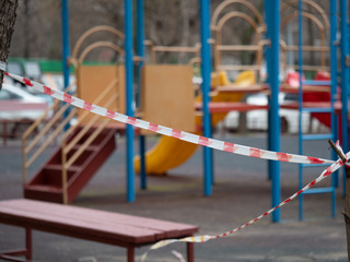 Fototapeta na wymiar Closed empty playground. Red and white barrier tape in focus. Quarantine. COVID-19