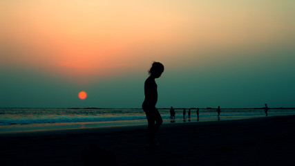 Fototapeta premium silhouette of a child on a sunset background in the sea or ocean on a beach in summer during vacation in Goa, India