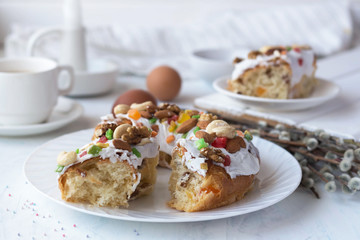 sweet bread with white icing, nuts and candied fruits lies on a plate, pastries