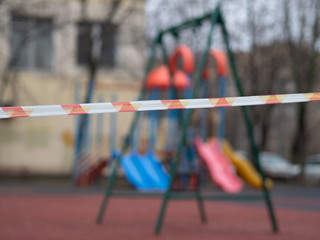 Closed empty playground.  Red and white barrier tape in focus. Quarantine. COVID-19