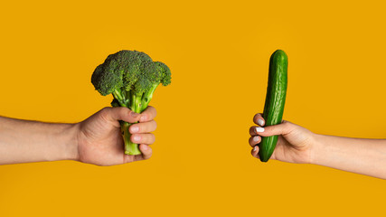 Fototapeta na wymiar Healthy eating. Closeup of man holding broccoli and woman with cucumber, orange background. Panorama