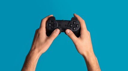 Lockdown activities. Millennial man holding video game controller on blue background, closeup. Panorama © Prostock-studio