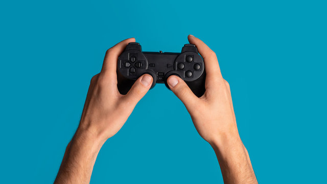 Lockdown activities. Millennial man holding video game controller on blue background, closeup. Panorama