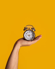 Time management. Young guy holding alarm clock on orange background, close up