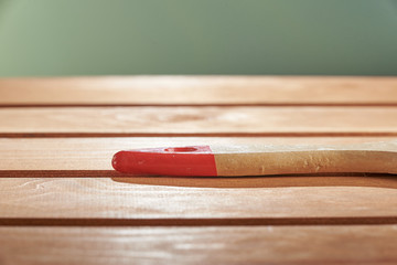 Freshly painted wood surface on a green background. The background is blurred. The wooden handle of the brush on the floor.