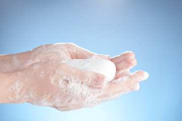 White soap in women's soapy hands on a blue background.