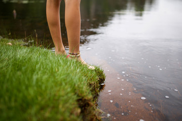 girl standing barefoot on grass by lake