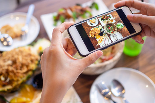 The girl's hand is taking pictures of the food on the table at home after ordering food online to eat at home. The concept of mobile phones to order food online