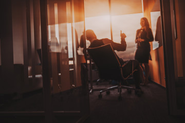 Defocused view of a modern boardroom with a silhouette of a male boss tumb up praising his female...
