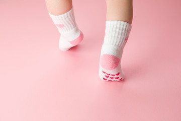 Baby going on light pink floor background. Pastel color. Feet in anti slip socks. Infant first...