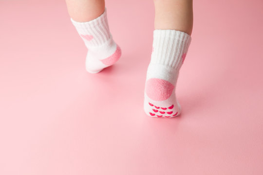 Baby going on light pink floor background. Pastel color. Feet in anti slip socks. Infant first steps. Closeup. Back view.