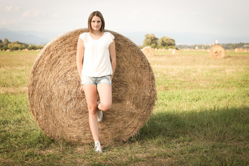 Naklejka na ściany i meble Blonde girl posing with a round bale, happy in nature, dressed in white