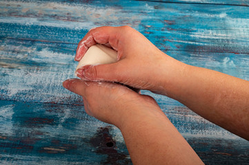 Someone is soaping their hands with a piece of toilet soap on a wooden background. Close up....