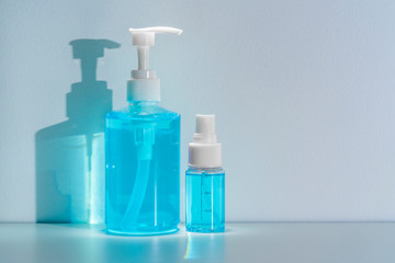 Bottles of blue anti-septic alcohol hand gel and spray on white table and casting blue shadow on white wall background