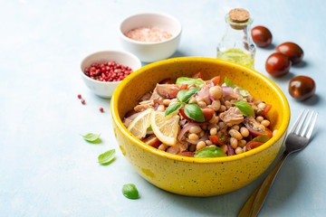 Healthy salad with tuna, white beans, cherry tomatoes, red onion and basil leaves in ceramic bowl on concrete background