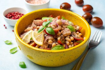Healthy salad with tuna, white beans, cherry tomatoes, red onion and basil leaves in ceramic bowl on concrete background