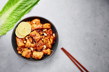 Fototapeta premium Korean Sweet Fried Chicken Dakgangjeong in black bowl at grey concrete background. Dakgangjeong is korean cuisine dish with deep fried crunchy chicken in sweet sauce. Korean Food