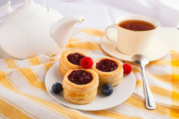 Cup of black tea with danish pastry cake with cranberry jam and fresh blueberry and raspberry on the table. Sunny breakfast.