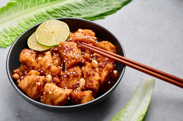 Korean Sweet Fried Chicken Dakgangjeong in black bowl at grey concrete background. Dakgangjeong is korean cuisine dish with deep fried crunchy chicken in sweet sauce. Korean Food