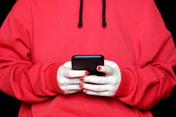 Young girl wearing in red hoodie looks to the screen of black smartphone photo on black background front close up