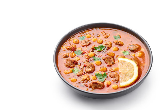 Moroccan Harira Soup in black bowl isolated on white bakcground. Harira is Moroccan Cuisine dish with lamb or beef meat, chickpeas, lentils, tomatoes and ciliantro. Ramadan Iftar Food. Copy space