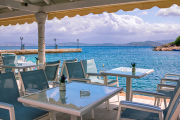 Landscape -  empty street café on the beach with view to the sea, pier, mountains on the horizon and blue sky.