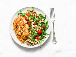 Healthy lunch - roasted chicken breast and white beans, arugula, cherry tomatoes salad on a light background, top view