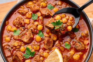 Moroccan Harira Soup in black bowl. Harira is Moroccan Cuisine dish with lamb or beef meat, chickpeas, lentils, tomatoes, ciliantro. Ramadan Iftar Food. Close up.