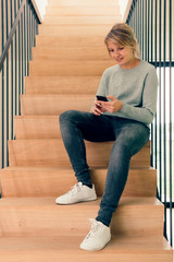 Girl at home using phone app sitting on the stairs - Young woman indoors using technology to...