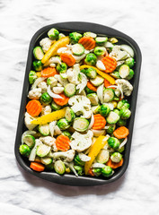 Raw ingredients for cooking vegetarian lunch seasonal vegetables - brussels sprouts, carrots, cauliflower, pumpkin, onion, sweet pepper on a baking tray on a light background, top view
